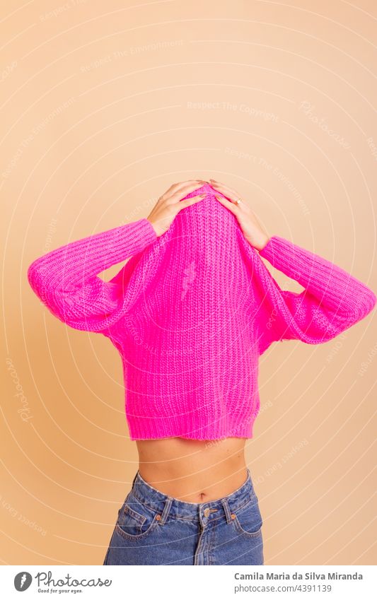 Porträt eines Mädchens mit einem schicken Pullover über dem Kopf, das Spaß hat. Frau mit gebundenem Haar, kalt, versteckt unter ihrem rosa Pullover. Mode-Foto.