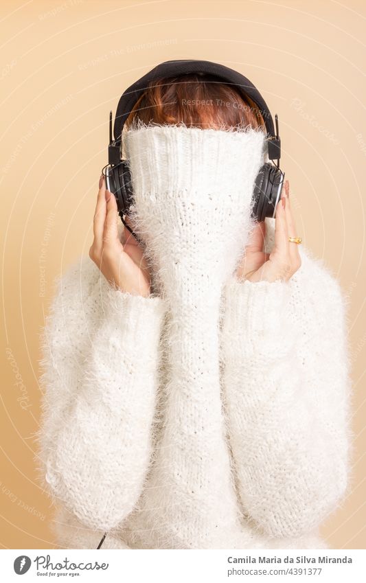Fun Porträt von Mädchen mit ihren trendigen weißen Pullover über den Kopf versteckt, kalt. Hört Musik mit Kopfhörern. Frau mit zusammengebundenem Haar. Foto im Studio.