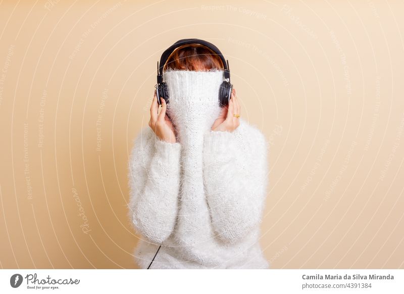 Fun Porträt von Mädchen mit ihren trendigen weißen Pullover über den Kopf versteckt, kalt. Hört Musik mit Kopfhörern. Frau mit zusammengebundenem Haar. Foto im Studio.