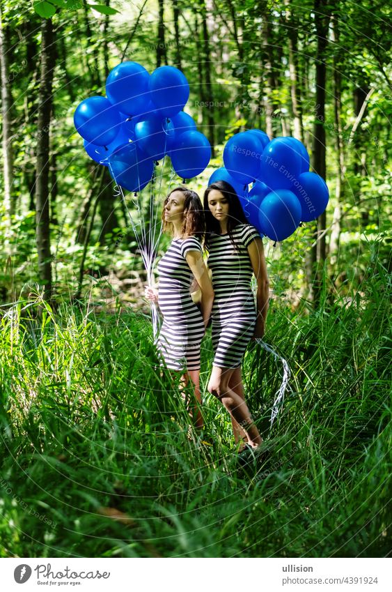 zwei frauen in schwarz-weiß gestreiftem kleid stehen mit blauen luftballons im wald hintereinander. künstlerische fotografie, copy space Haufen Helium frei Halt