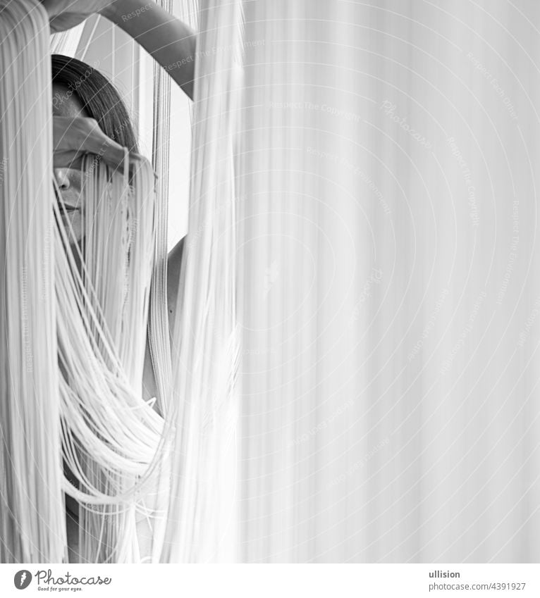Porträt einer jungen attraktiven Frau mit unbedeckten Schultern, die mit den Händen dekorativ an den Fäden eines Vorhangs zieht, in schwarz-weiß. Bild mit Kopierraum, Platz für Text.