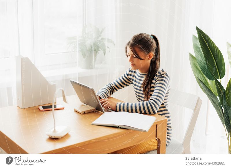Eine dunkelhaarige Schülerin sitzt an einem Schreibtisch und macht mit ihrem Tablet ihre Hausaufgaben. Moderne Technologien, Online-Bildung, Ausbildung