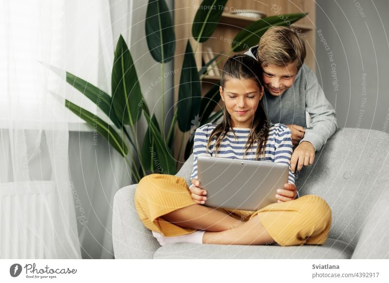 Die Schwester und der ältere Bruder sitzen zu Hause auf einem Stuhl und spielen auf einem Tablet. Moderne Technik und Zeit zu Hause verbringen heimwärts