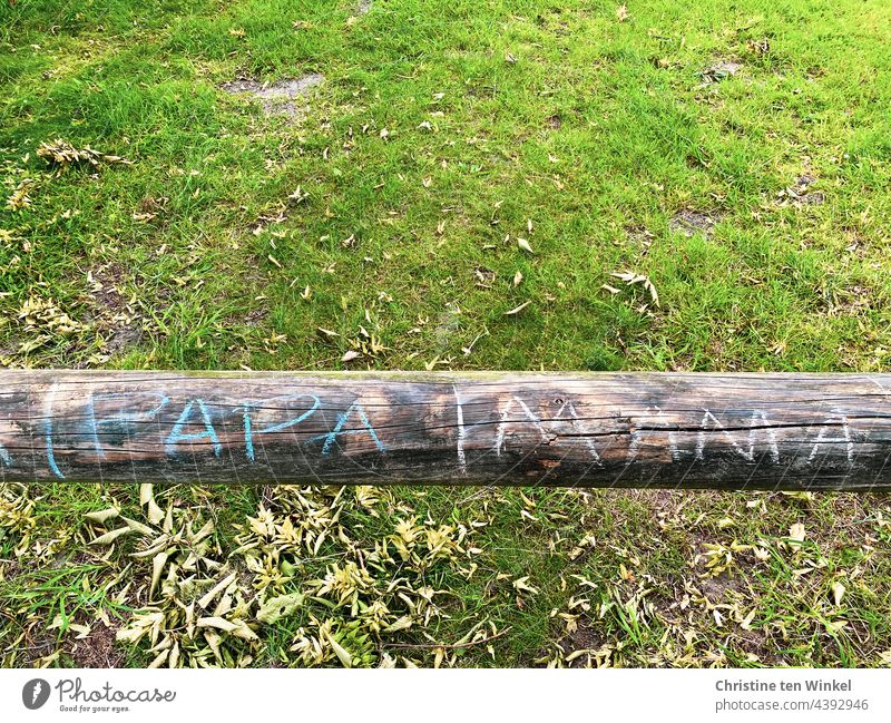 |PAPA|MAMA steht mit bunter Kreide geschrieben auf einem Rundholz / Holzbalken, der als Absperrung vor einem leeren Grundstück dient Mama Papa Kreideschrift