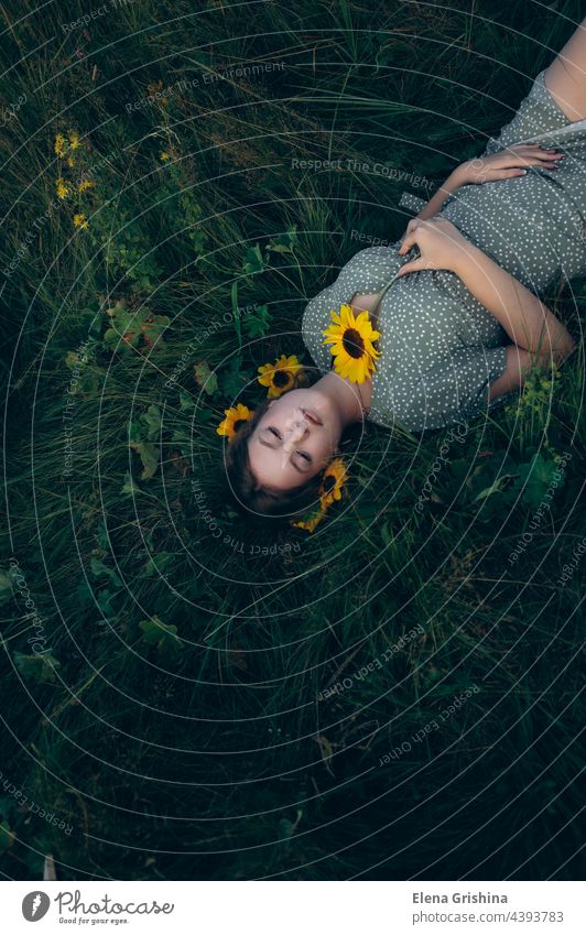 Porträt eines jungen Mädchens, das im Gras zwischen Blumen liegt. Sonnenblume Kleid Sommer schön Weiblichkeit Lächeln Behaarung anketten Schmuckanhänger