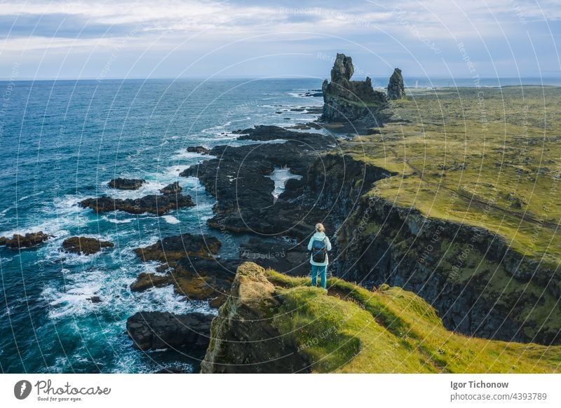 Ein Wanderer in gelber Jacke steht auf dem Gipfel eines Felsens in einem Outdoor-Park in Island. Londrangar Küste Halbinsel Snæfellsnes Lava Formationen MEER