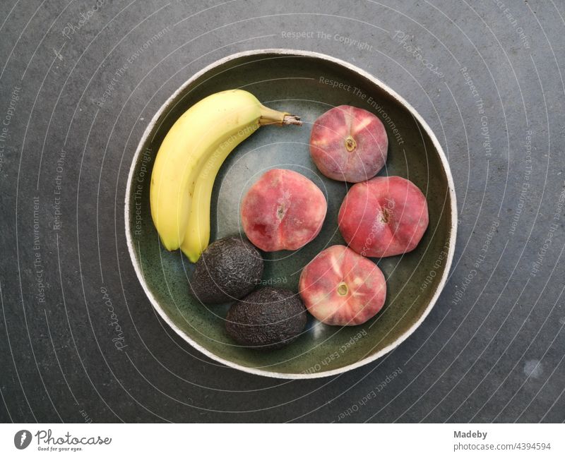 Runde Obstschale mit Banane, Pfirsich und Avocado auf grauem Betonboden in einer Designerwohnung in Rudersau bei Rottenbuch im Kreis Weilheim-Schongau in Oberbayern