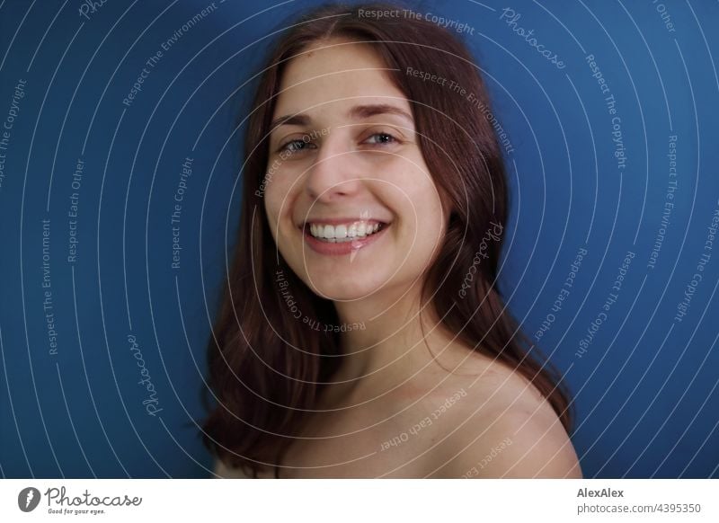 Junge Frau mit Grübchen lächelt und schaut in die Kamera, während sie vor einer petrolblauen Wand steht brünett sportlich 18-30 Jahre Erwachsene langhaarig