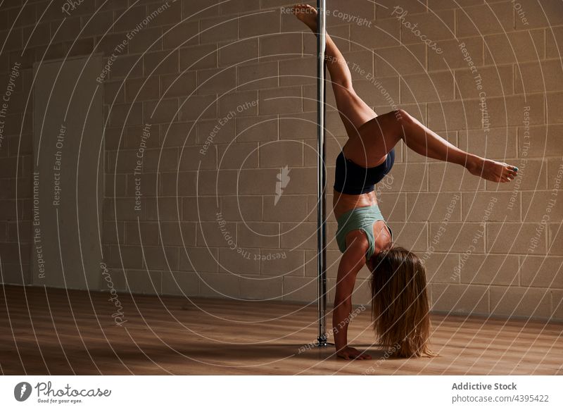 Anonyme Pole-Tänzerin beim Handstand im Studio Frau Tanzen Mast beweglich Probe Anmut Atelier gymnastisch Pylon akrobatisch Handstand Pfeil und Bogen