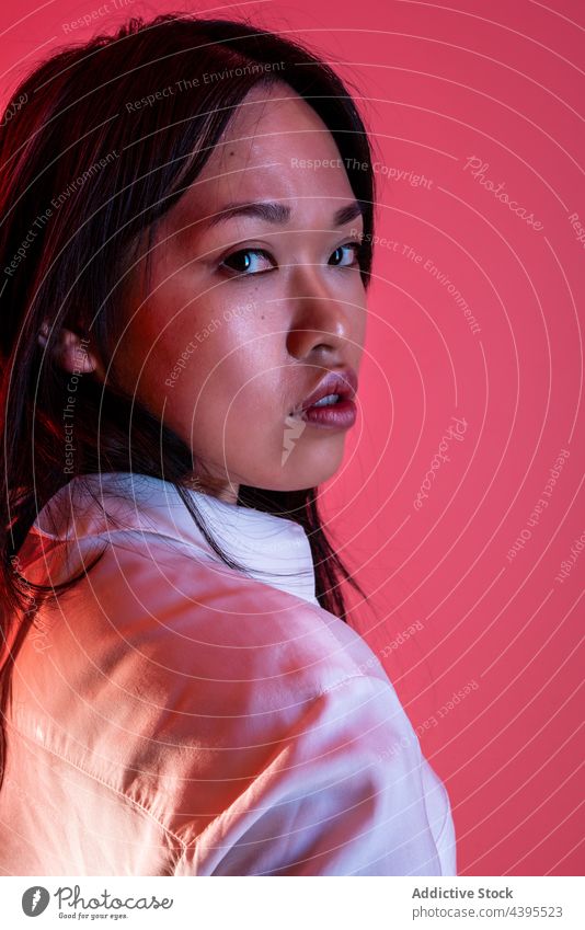 Stilvolle asiatische Frau im Studio auf rosa Hintergrund Model trendy Atelier selbstbewusst Vorschein Outfit ernst ethnisch Individualität Bekleidung