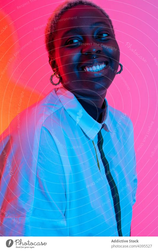 Fröhliche schwarze Frau im Studio mit Neonlicht neonfarbig Atelier Licht heiter Model Lächeln Stil trendy farbenfroh Afroamerikaner ethnisch Inhalt Freude Glück