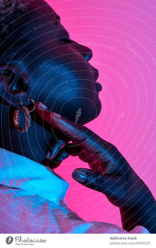 Zarte schwarze Frau mit stilvollem Schmuck im Studio Model Stil Accessoire Ohrringe neonfarbig Licht trendy ethnisch Afroamerikaner Atelier Angebot kreativ hell