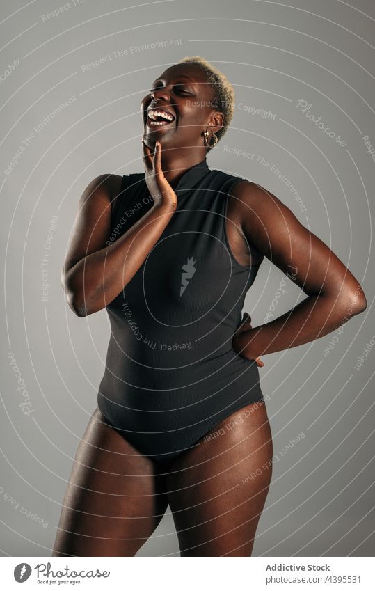 Glückliche schwarze Frau im Bodysuit im Studio körperpositiv heiter Lachen Körper Kurve Form Freude ethnisch Afroamerikaner Augen geschlossen Optimist froh