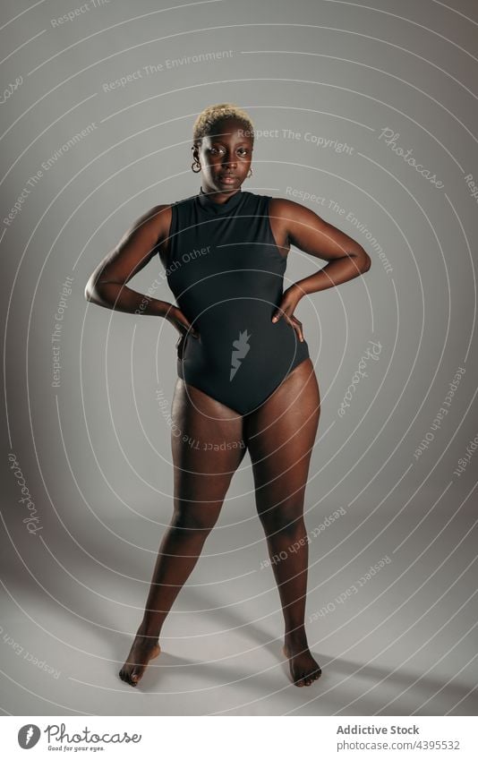 Ernste Frau mit den Händen auf den Hüften im Bodysuit im Studio körperpositiv Körper Kurve Form Freude ethnisch Afroamerikaner schwarz Optimist froh Inhalt