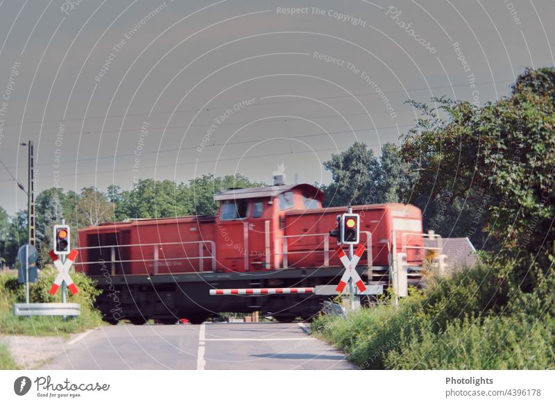 Rote Eisenbahn an einem Bahnübergang mit Schranke und Warnleuchte Licht rot Warnlicht Andreaskreuz fahren Verkehr Gleise Bahnfahren Schienenverkehr