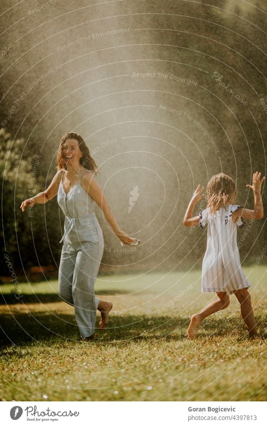 Niedliches kleines Mädchen, das sich mit seiner Mutter unter dem Sprinkler vergnügt aktiv Aktivität Vergnügen Hinterhof heiter Kind Kindheit Tag Tropfen