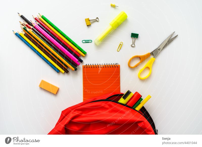 Ein roter Schulrucksack gefüllt mit Buntstiften, einer Schere und einem Notizblock Schultasche Rucksack Schule Bildung Farbstift notizblock weißer Hintergrund