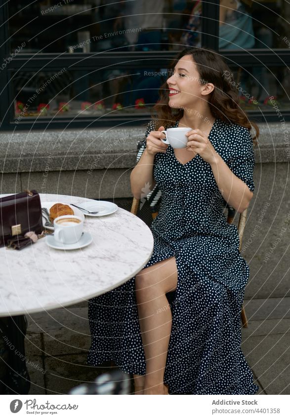Stilvolle Frau mit Milchkaffee in einem Straßencafé Latte Kaffee Heißgetränk Getränk Gebäck Kleid Beine gekreuzt Café Punktmuster elegant gepunktet Ornament