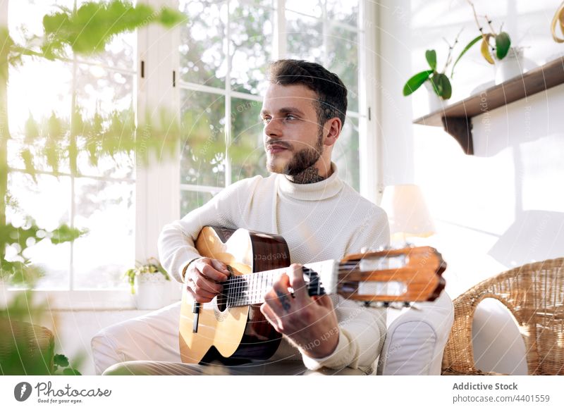 Gitarrist spielt Akustikgitarre im Sessel zu Hause Gitarrenspieler spielen Musik klassisch Kunst Klang nachdenken heimwärts Mann Armsessel akustisch Schnur