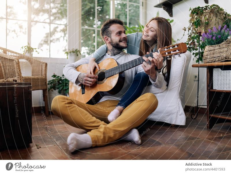 Lächelnder Gitarrist, der Gitarre spielt, während er sich mit seiner Freundin zu Hause unterhält Gitarrenspieler spielen interagieren Partnerschaft Liebe Musik