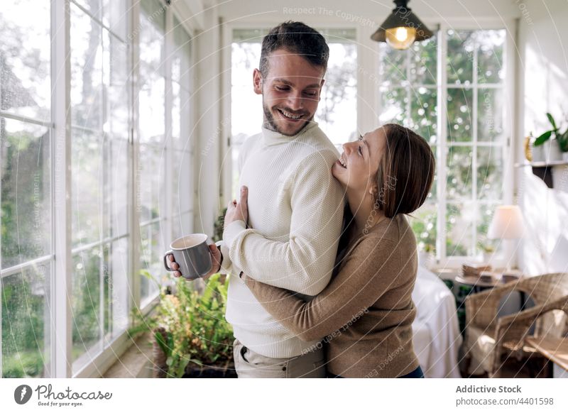 Lächelnde Frau, die ihren tätowierten Freund zu Hause umarmt Paar Umarmen Liebe Partnerschaft romantisch nachdenken Kaffee Tattoo Fenster heiter interagieren