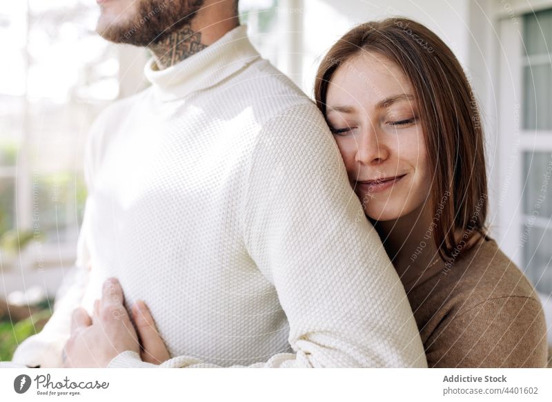 Lächelnde Frau, die ihren tätowierten Freund zu Hause umarmt Paar Umarmen Liebe Partnerschaft romantisch nachdenken Tattoo Fenster heiter interagieren heimwärts