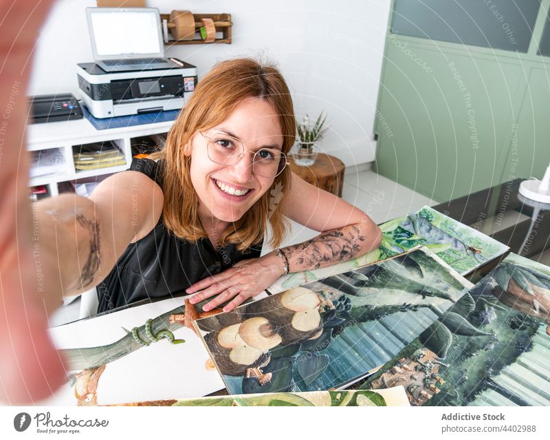 Lächelnde Künstlerin macht Selfie im Kreativstudio Frau Designer heiter Selbstportrait Smartphone Anstreicher Werkstatt benutzend Apparatur Gerät fotografieren