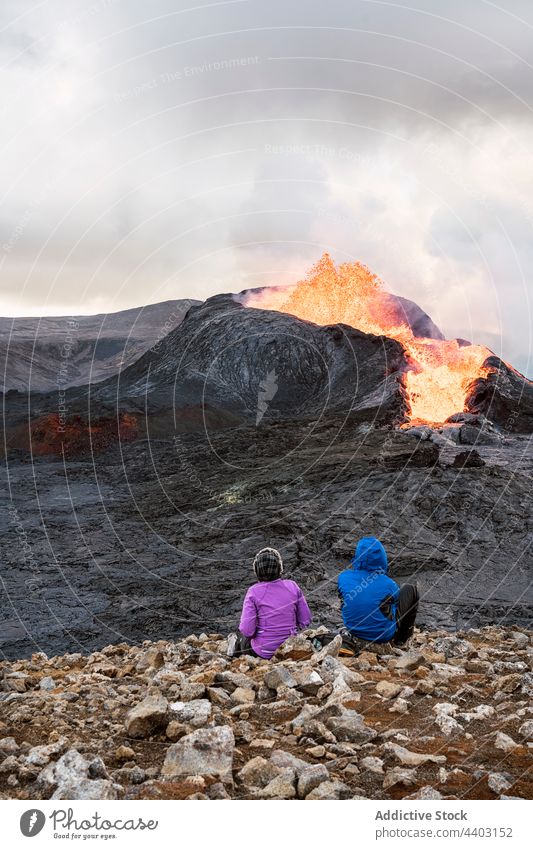 Gesichtslose Touristen, die vom Berg aus einen aktiven Vulkan unter bewölktem Himmel betrachten bewundern ausbrechen Brandwunde Feuer Reittier Natur Energie