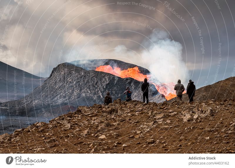 Gesichtslose Touristen, die vom Berg aus einen aktiven Vulkan unter bewölktem Himmel betrachten bewundern ausbrechen Brandwunde Feuer Reittier Natur Energie