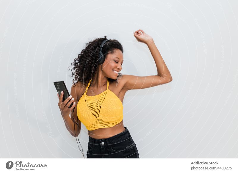 Fröhliche schwarze Frau mit Headset und Smartphone tanzt zu Musik Tanzen Kopfhörer zuhören Glück Gesang freie Zeit benutzend Apparatur Gerät Funktelefon Draht