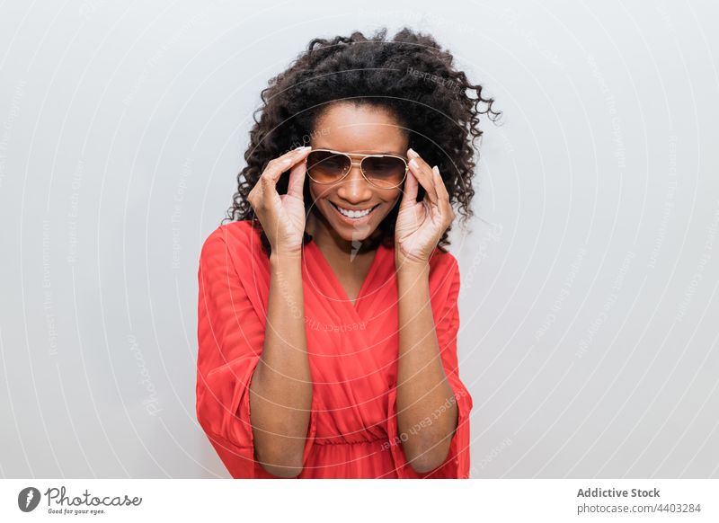 Modisches schwarzes Modell mit Sonnenbrille auf hellem Hintergrund trendy Individualität feminin Design krause Haare Frau Porträt stylisch kreativ Stil rot
