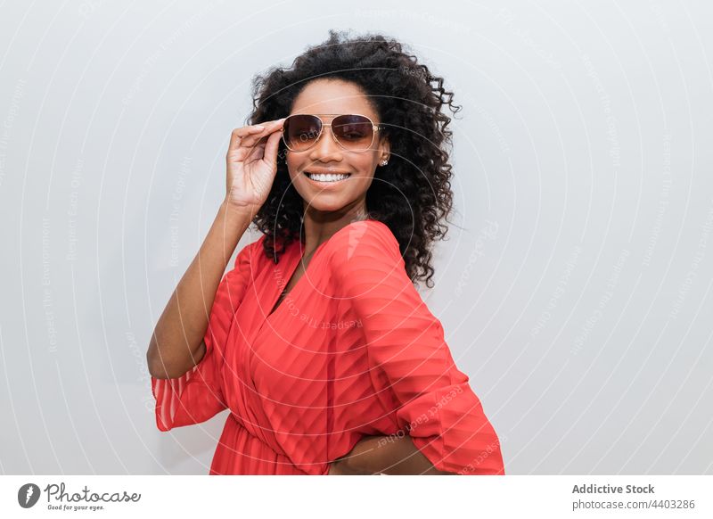 Modisches schwarzes Modell mit Sonnenbrille auf hellem Hintergrund trendy Individualität feminin Design krause Haare Frau Porträt stylisch kreativ Stil rot