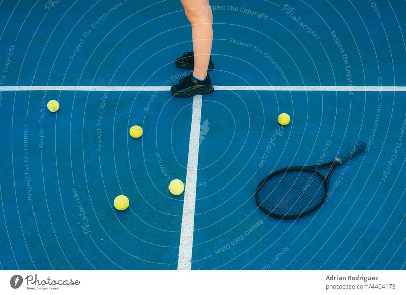 Detail Füße einer anonymen Frau auf einem bunten Tennisplatz mit Schläger und Tennisbällen darauf Ball Remmidemmi Wettbewerbe Freizeitaktivitäten Freizeitsport