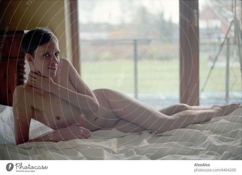 Analoges Akt- Portrait einer jungen Frau auf einem Bett vor einem Balkonfenster intensiv schauen Erwartung Emotion Laken Gegenlicht Ausdruck Tripod Körnung 35mm