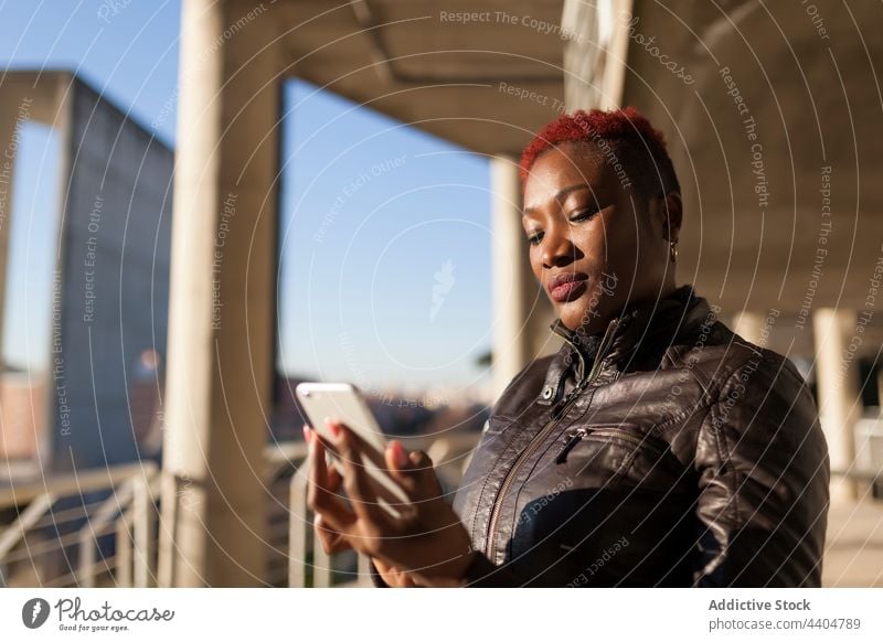 Afro-Frau beim Surfen mit ihrem Smartphone schwarz Afro-Look ethnisch App Tippen Mädchen trendy Blick Lifestyle Erwachsener offen Hintergrund benutzend urban