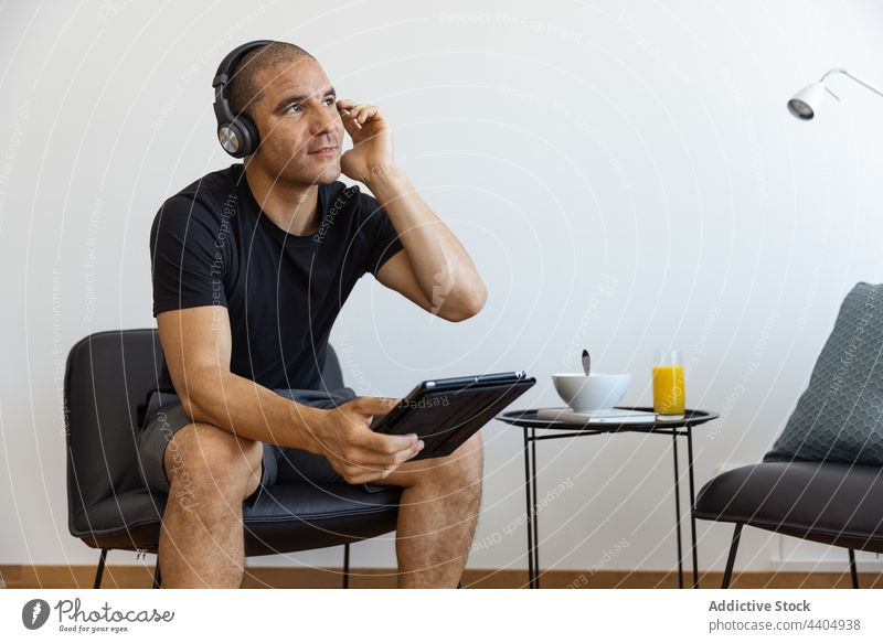 Zufriedener Mann benutzt Tablet zu Hause zuschauen Tablette benutzend Video heimwärts Morgen männlich Browsen Surfen sitzen Anschluss Apparatur Gerät Internet