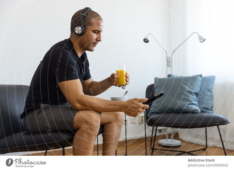 Zufriedener Mann, der zu Hause Saft trinkt und eine Tablette benutzt zuschauen benutzend Video trinken orange heimwärts Morgen männlich Browsen Surfen sitzen