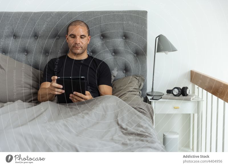 Mann surft morgens im Bett auf seinem Tablet Browsen Tablette Morgen wach Schlafzimmer benutzend Surfen online männlich heimwärts Apparatur Gerät Komfort