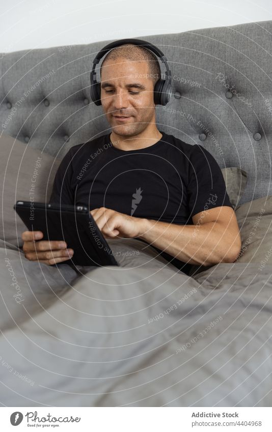 Mann benutzt morgens zu Hause im Bett ein Tablet Morgen Browsen benutzend Tablette zuhören Musik Schlafzimmer wach männlich Apparatur ruhen Gerät
