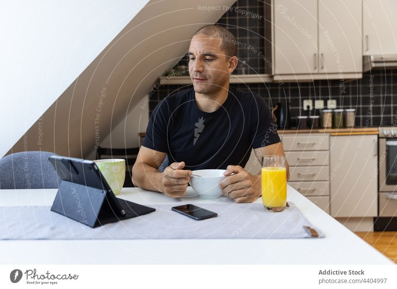 Mann surft während des Frühstücks zu Hause auf einem Tablet heimwärts Browsen Tablette benutzend Morgen Lebensmittel Surfen online männlich Apparatur Internet