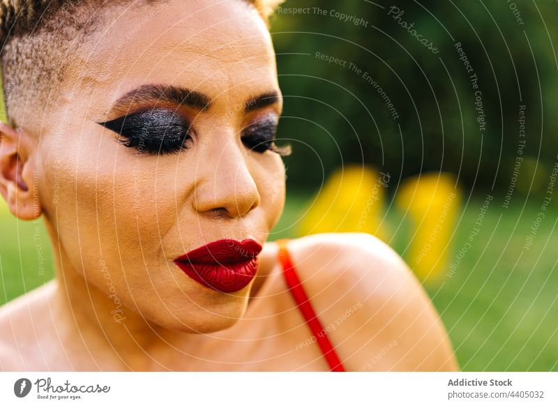 Stilvolle schwarze Frau mit Make-up Porträt geschlossene Augen Individualität selbstbewusst Haarschnitt Park festlich anhaben rot Farbe hell Afroamerikaner