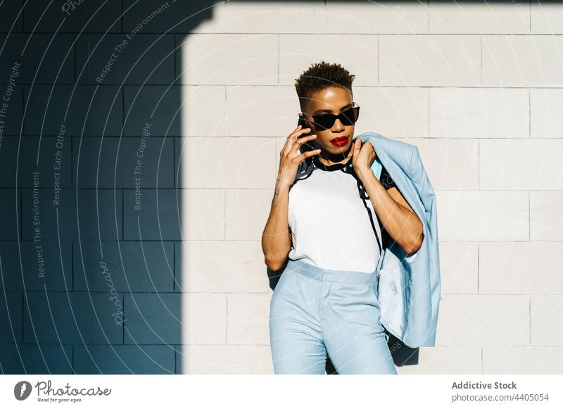 Trendige ethnische Frau mit Sonnenbrille, die auf der Straße mit ihrem Smartphone spricht Mode Stil reden Individualität cool Haarschnitt benutzend Apparatur