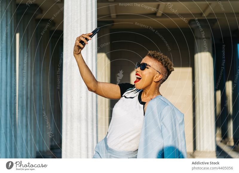 Trendige ethnische Frau mit Sonnenbrille nimmt Selfie auf Smartphone auf der Straße Mode Stil Individualität cool heiter Lächeln Glück Haarschnitt benutzend