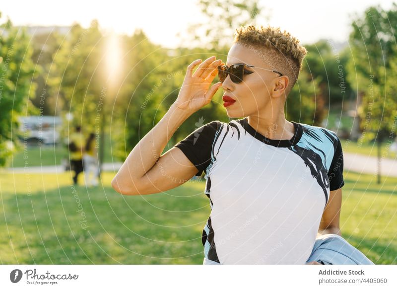 Stilvolle schwarze Frau mit Sonnenbrille auf einer Bank im Park Mode trendy Individualität cool Haarschnitt nachdenken Straßenbelag stylisch Fliesen u. Kacheln