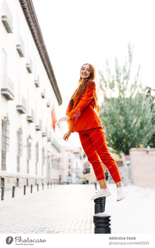 Elegante Frau steht auf Parkpoller in der Stadt Stil orange Anzug trendy Großstadt Straße parken Poller lebhaft Farbe hell stehen Gleichgewicht Mode urban