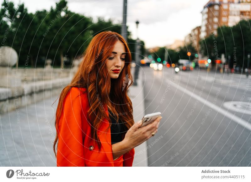 Rothaarige Frau beim Surfen auf dem Smartphone in der Stadt soziale Netzwerke orange Anzug pulsierend Mobile Apparatur Telefon Gerät rote Haare Rotschopf Ingwer
