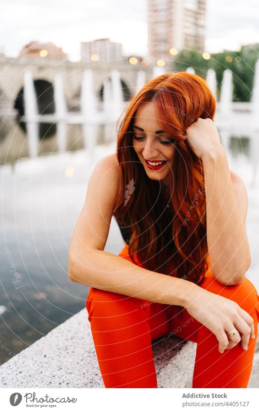 Trendige rothaarige Frau auf dem Deich in der Stadt Rotschopf Stil Stauanlage Großstadt trendy Hose orange hell Farbe sich auf die Hand lehnen lebhaft