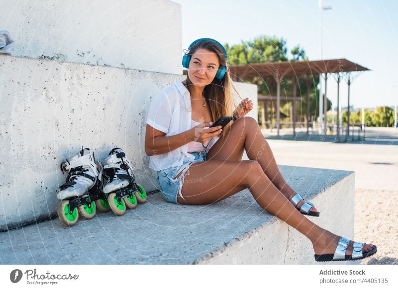 Lächelnde Frau, die auf der Straße auf ihrem Smartphone surft und Kopfhörer benutzt Großstadt Sommer Moment Glück heiter Text Nachricht Browsen Mobile Gerät
