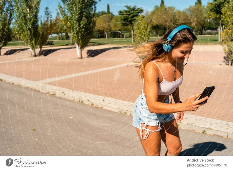 Fröhliche Frau beim Rollerbladen und mit Smartphone zuhören Musik benutzend Großstadt Sommer Skater Mitfahrgelegenheit Gerät Apparatur heiter Glück Internet