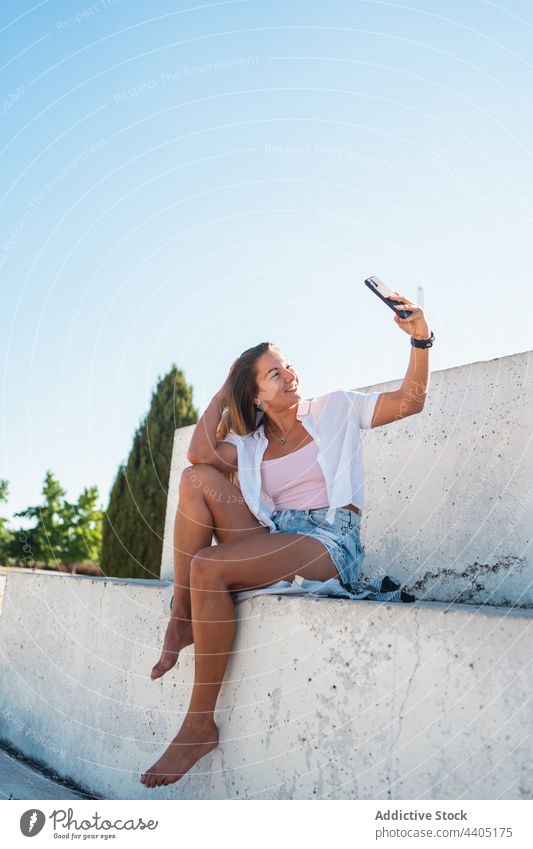 Lächelnde Frau nimmt Selfie auf der Straße Smartphone Großstadt Sommer Selbstportrait Moment Glück heiter Gedächtnis Mobile Gerät Funktelefon fotografieren